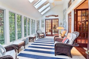 Bright sunroom with large windows, skylights, wicker furniture, striped blue and white rug, and a view of greenery outside, presented by Crown Point Realtors.