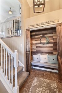 Cozy stair nook under a wooden staircase in Northwest Indiana, decorated with cushions, a wreath, and a quote saying "happiness is being near your best friend.