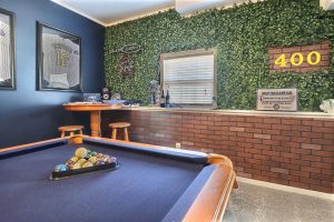 A sports-themed game room with a pool table, artificial grass wall, sports memorabilia, and neon signs, perfect for Crown Point Realtors to unwind.